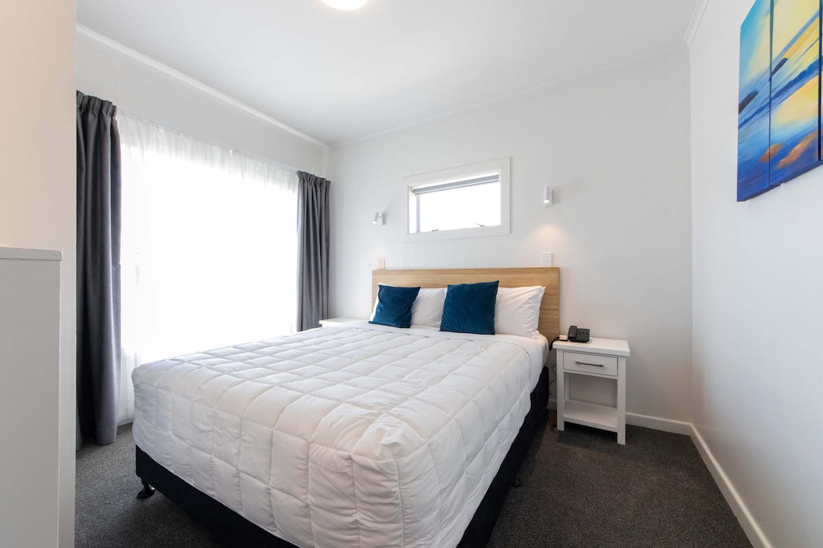 A neatly arranged hotel room with a large bed, a bedside table, and a window with curtains.