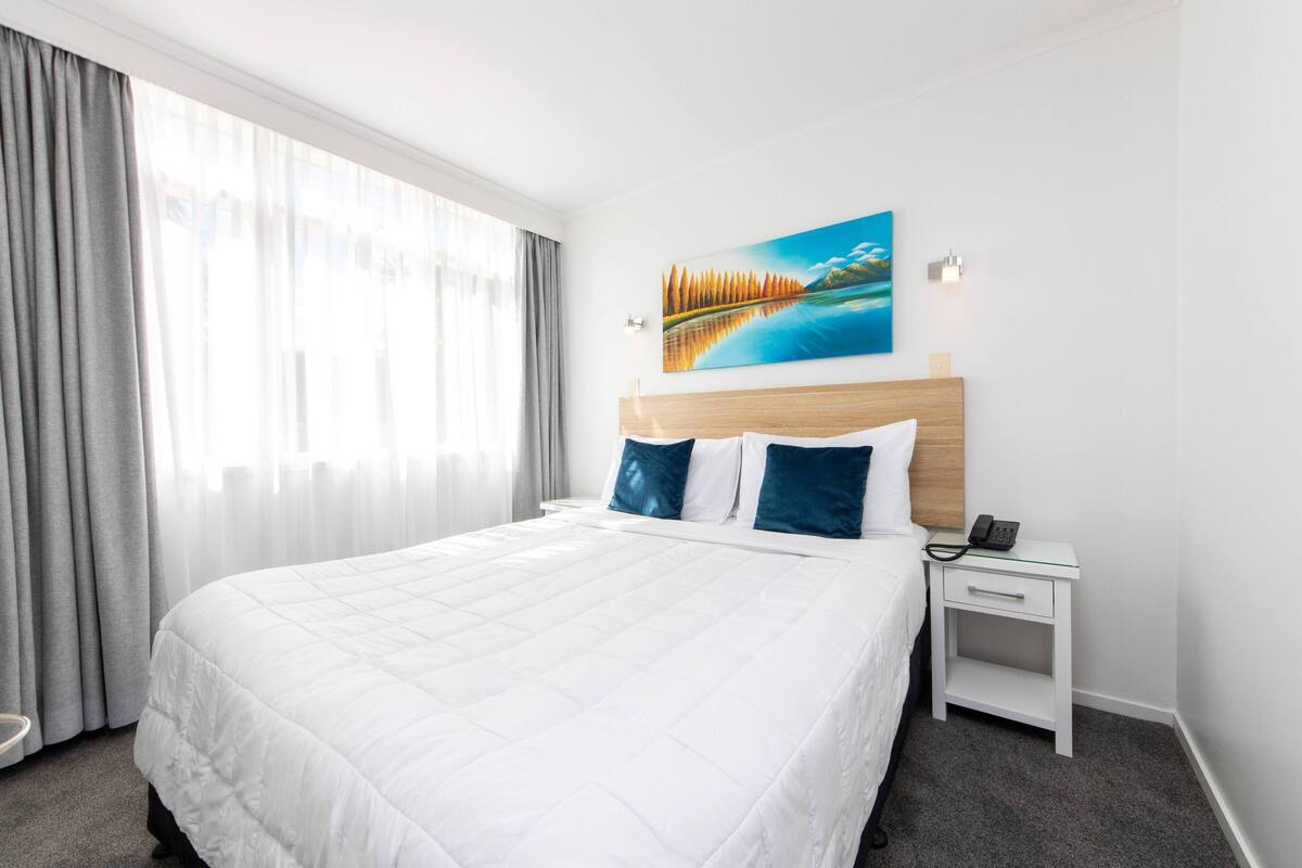 A hotel room with a large bed, a nightstand with a phone, and a painting on the wall.