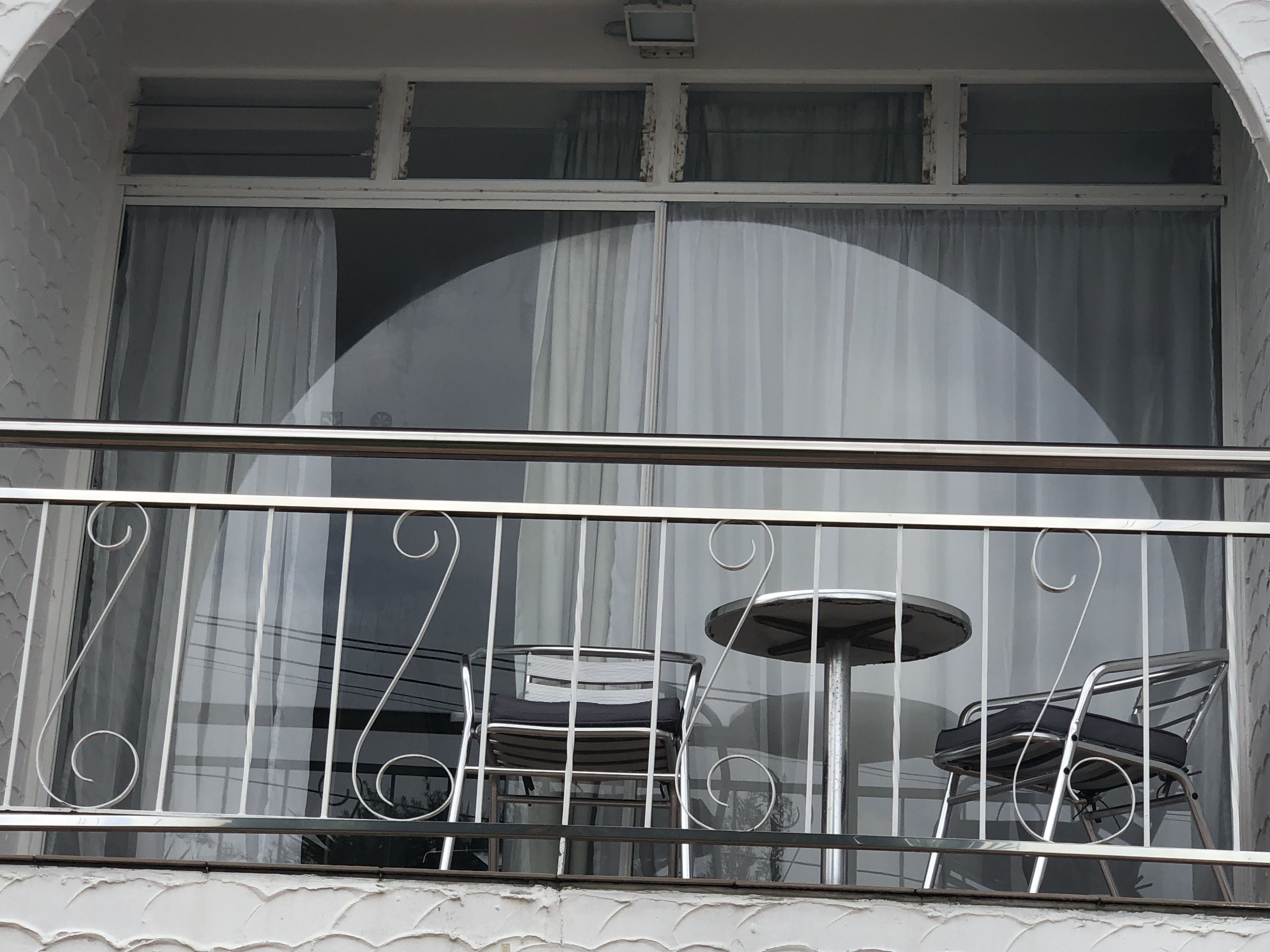 Een balkon met een metalen hekwerk, een tafel en twee stoelen.