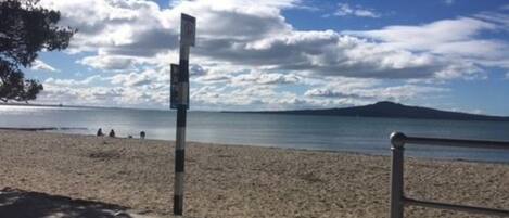 Una playa con una baranda metálica y un cartel.