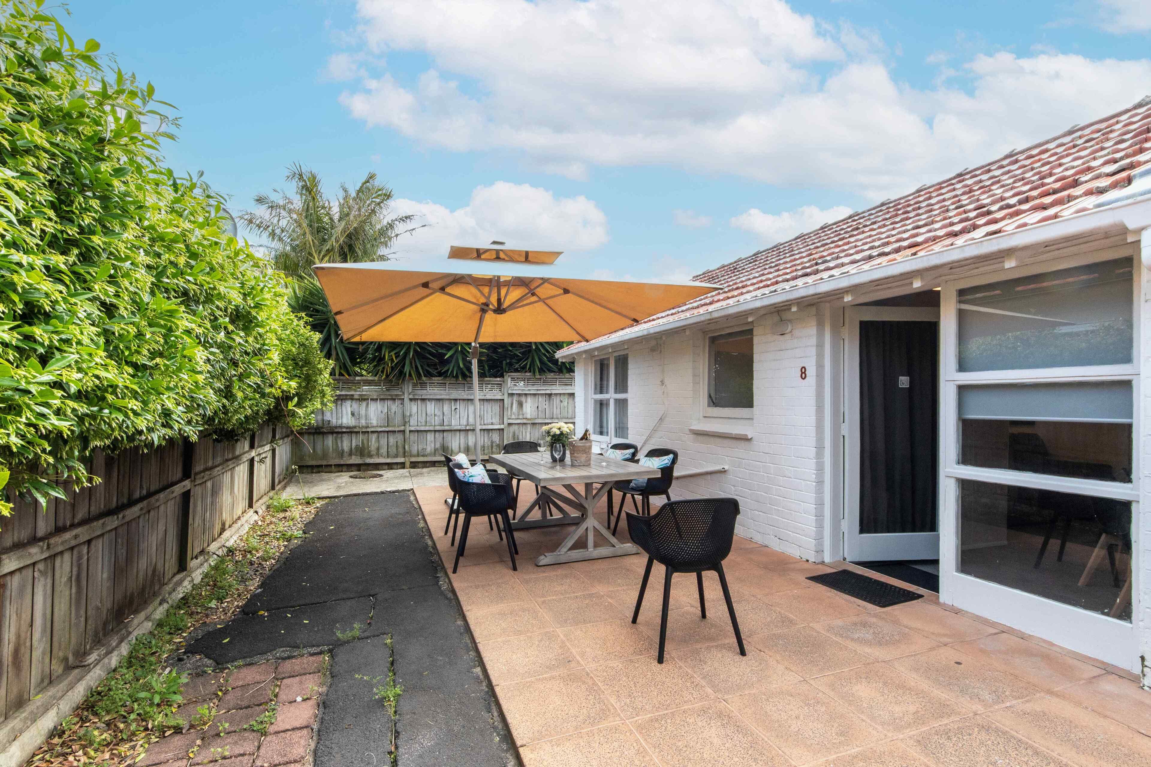A patio with a table and chairs, a wooden fence, and a house with a tiled roof.