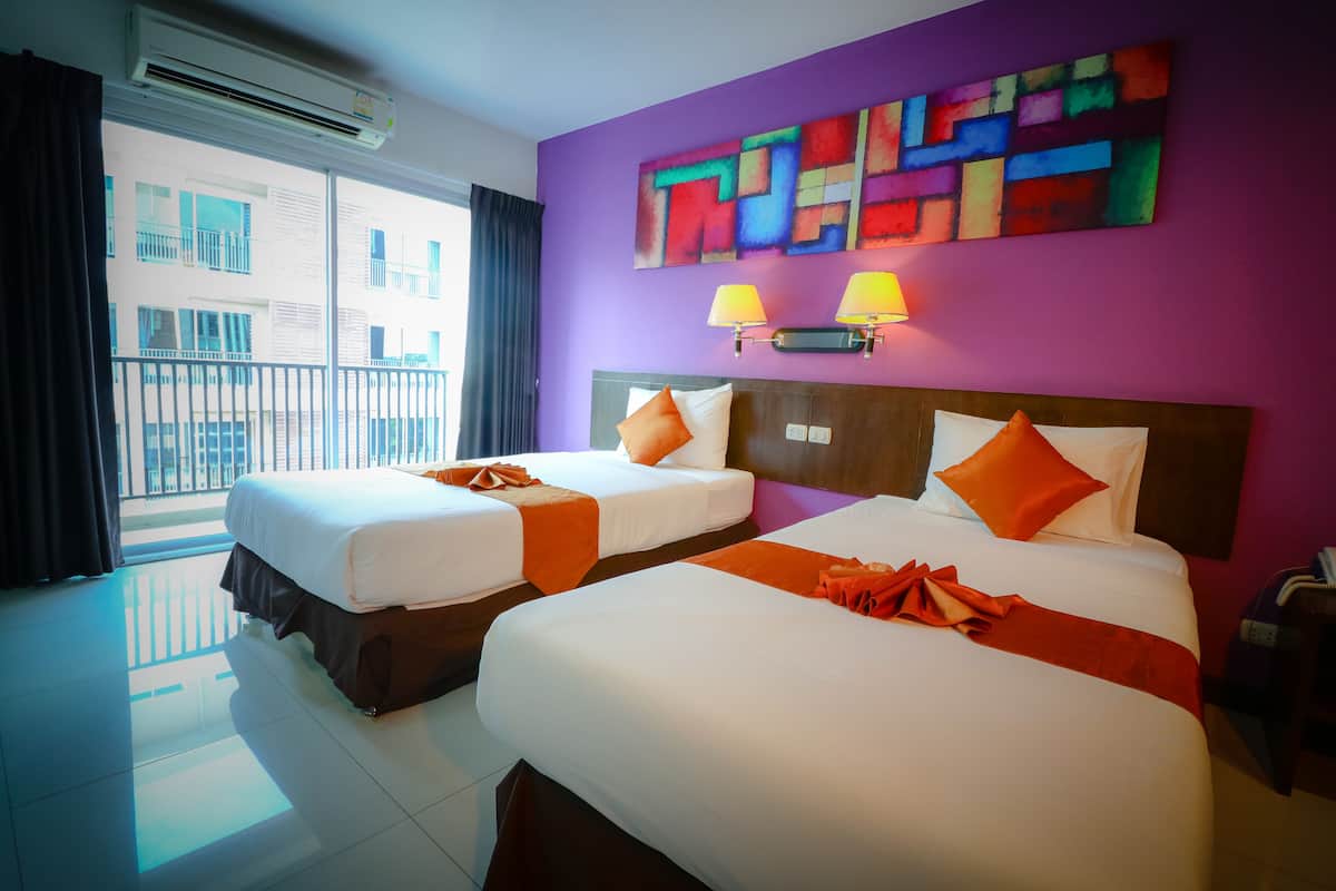 Habitación de hotel con dos camas, vista al balcón, un cuadro abstracto de colores y un teléfono en la mesita de noche.