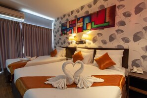 Une chambre d’hôtel avec deux lits, chacun recouvert d’une couvre-lit et doté d’oreillers orange, et une décoration en forme de cœur faite de serviettes sur le lit, au premier plan. Un tableau abstrait et coloré est accroché au mur au-dessus des lits, et un téléphone se trouve sur une table de chevet.
