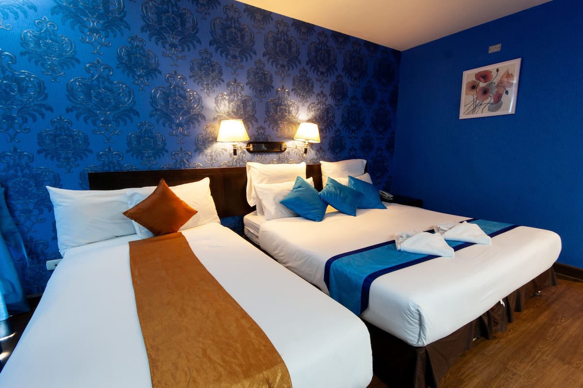Habitación de hotel con dos camas, papel tapiz azul con estampado y dos lámparas fijadas a la pared.