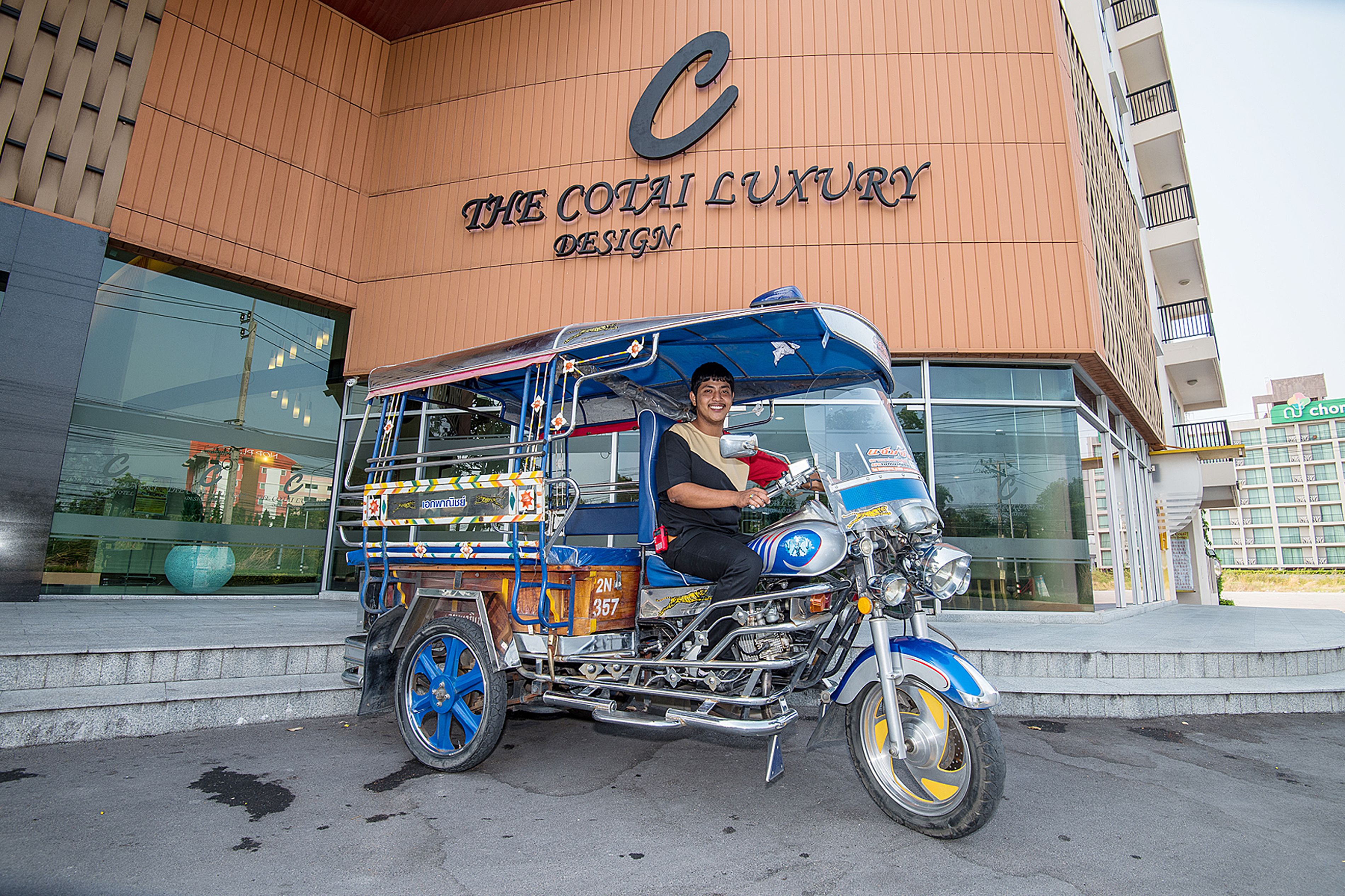 A motorcycle with a blue and yellow color scheme parked in front of a building with a sign that reads "The Coti Air Luxury Design".