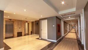 Un couloir d’hôtel moderne, doté d’ascenseurs, d’un sol recouvert de moquette et d’une porte portant le numéro 7.