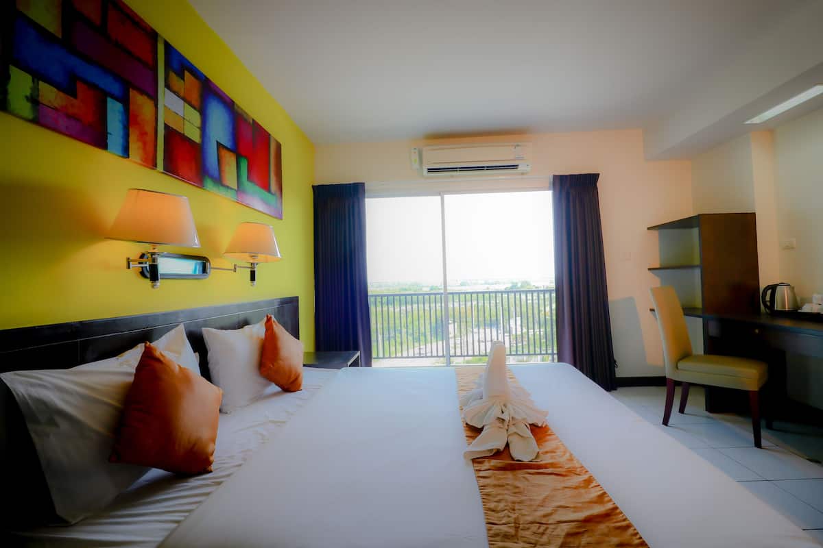 Habitación de hotel con una cama grande, un escritorio, una silla y un balcón con vistas.