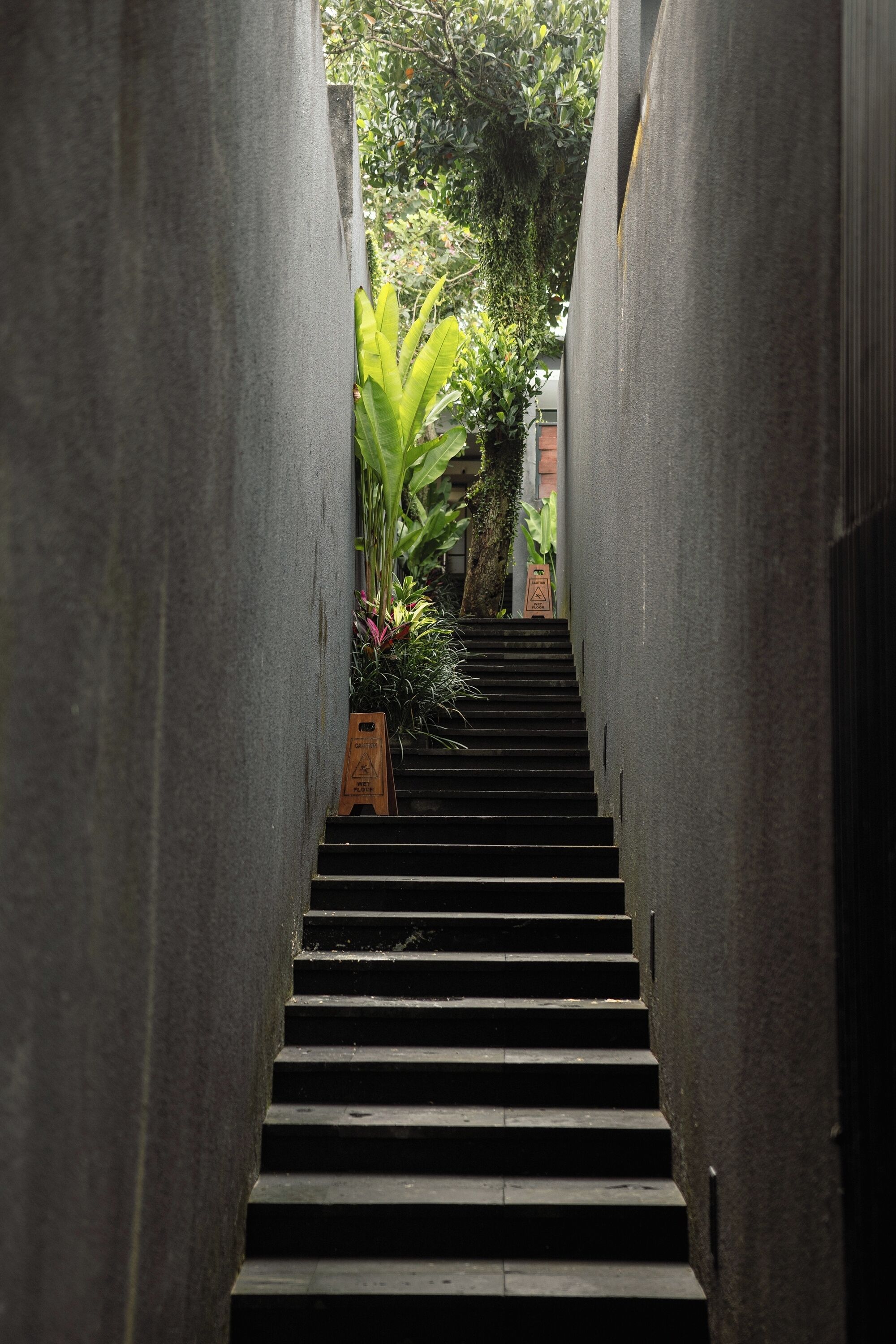 Una escalera estrecha bordeada por paredes de concreto, que lleva a una puerta con un letrero de precaución.
