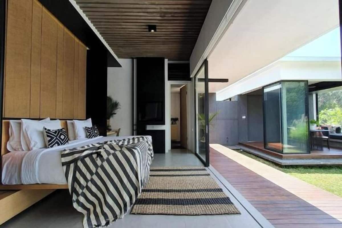 A modern bedroom with a bed, a TV, and a view of the outdoor patio.