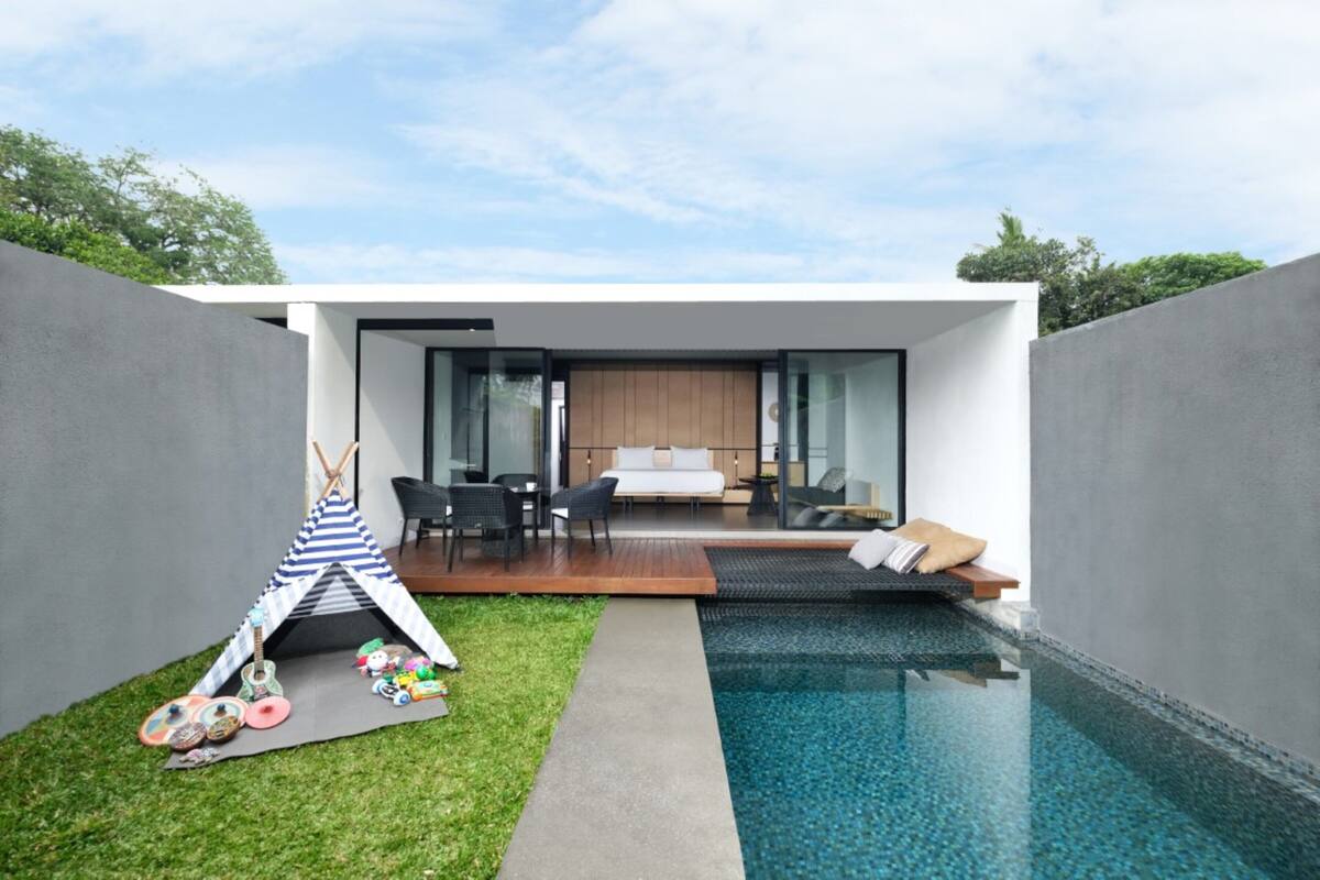 A modern outdoor pool area with a glass-enclosed bedroom and a small play area with a teepee and toys.