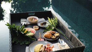 Una bandeja flotante con comida y bebidas sobre una piscina, rodeada de follaje y un muro de hormigón.
