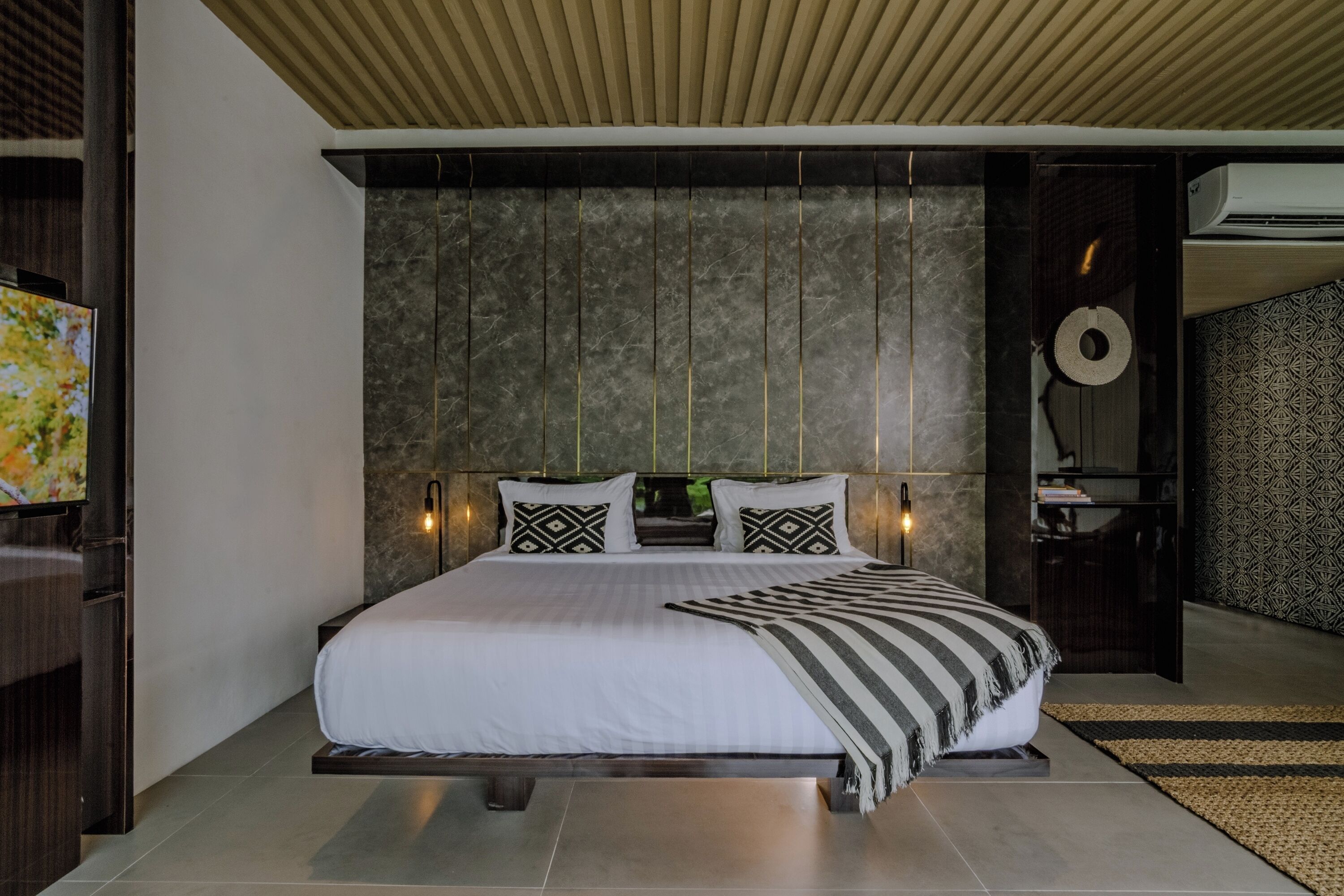 A modern bedroom with a large bed, a television, and a wall-mounted air conditioning unit.