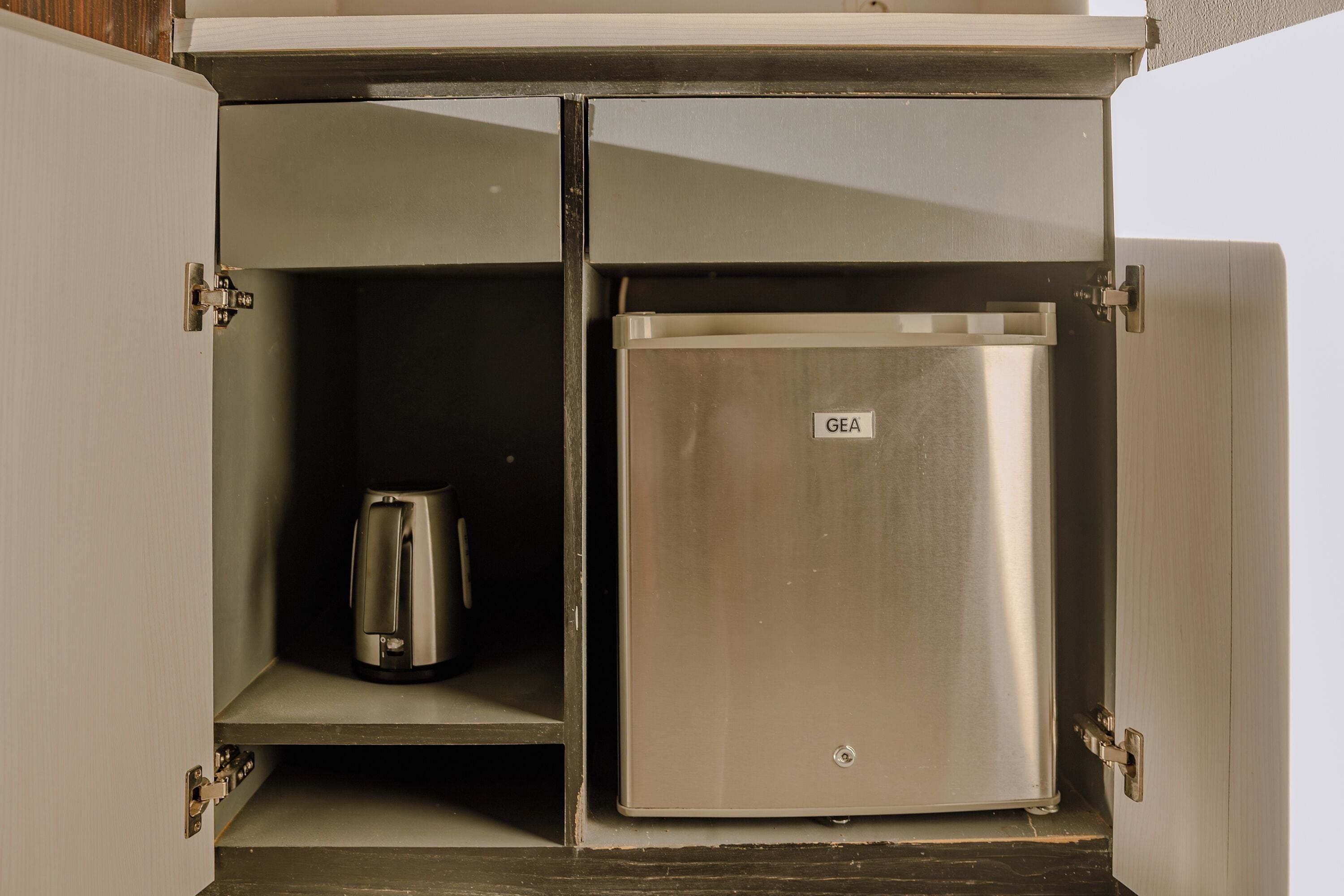 Un refrigerador metálico compacto con el logotipo de GE, una cafetera y un estante pequeño dentro de un mueble de cocina.