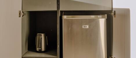 Un refrigerador metálico compacto con el logotipo de GE, una cafetera y un estante pequeño dentro de un mueble de cocina.