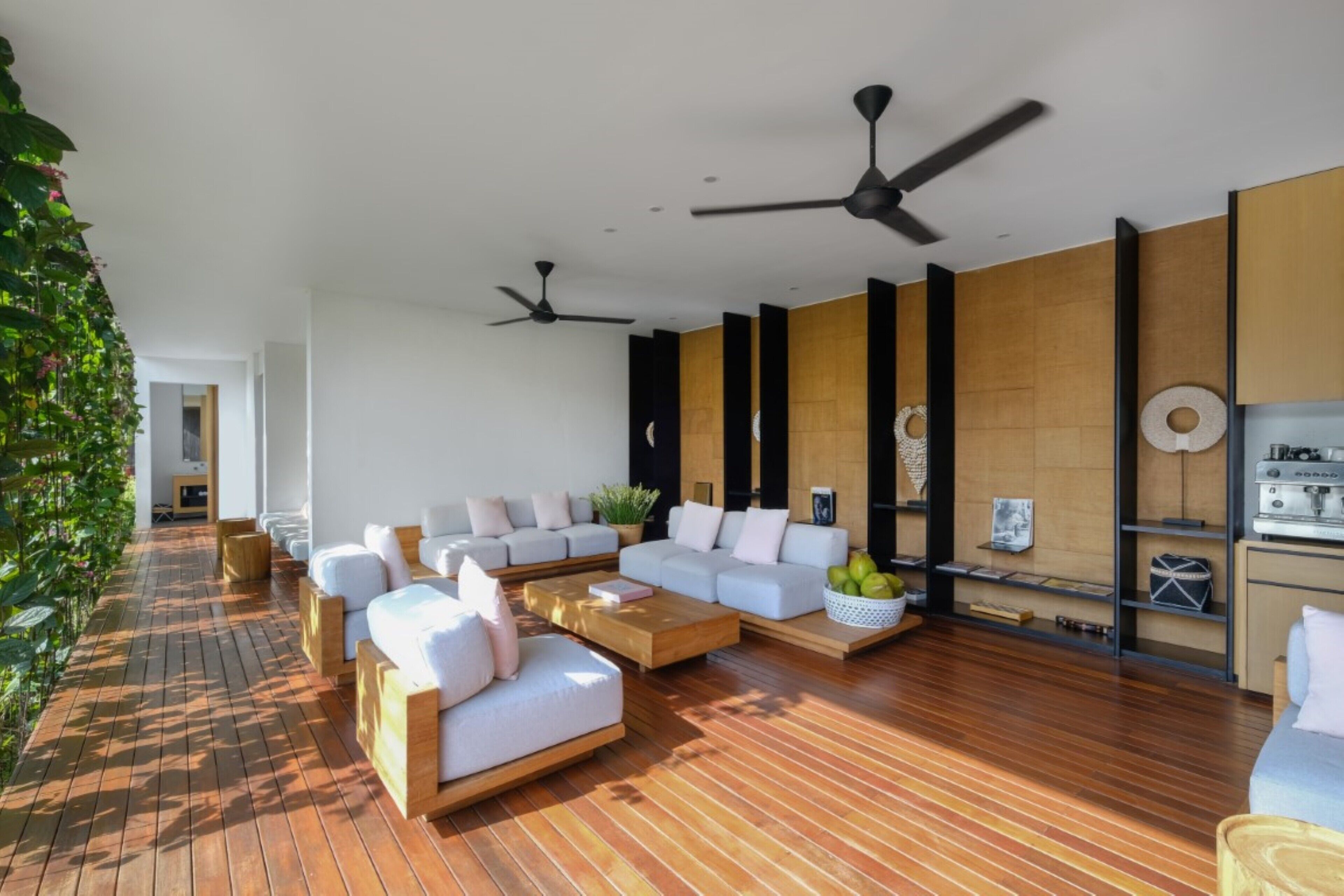 A modern living room with a wooden floor, white sofas, a coffee table, and ceiling fans.