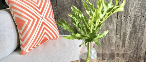 A vase with green leaves on a wooden tray, a gray sofa, and an orange and white pillow.