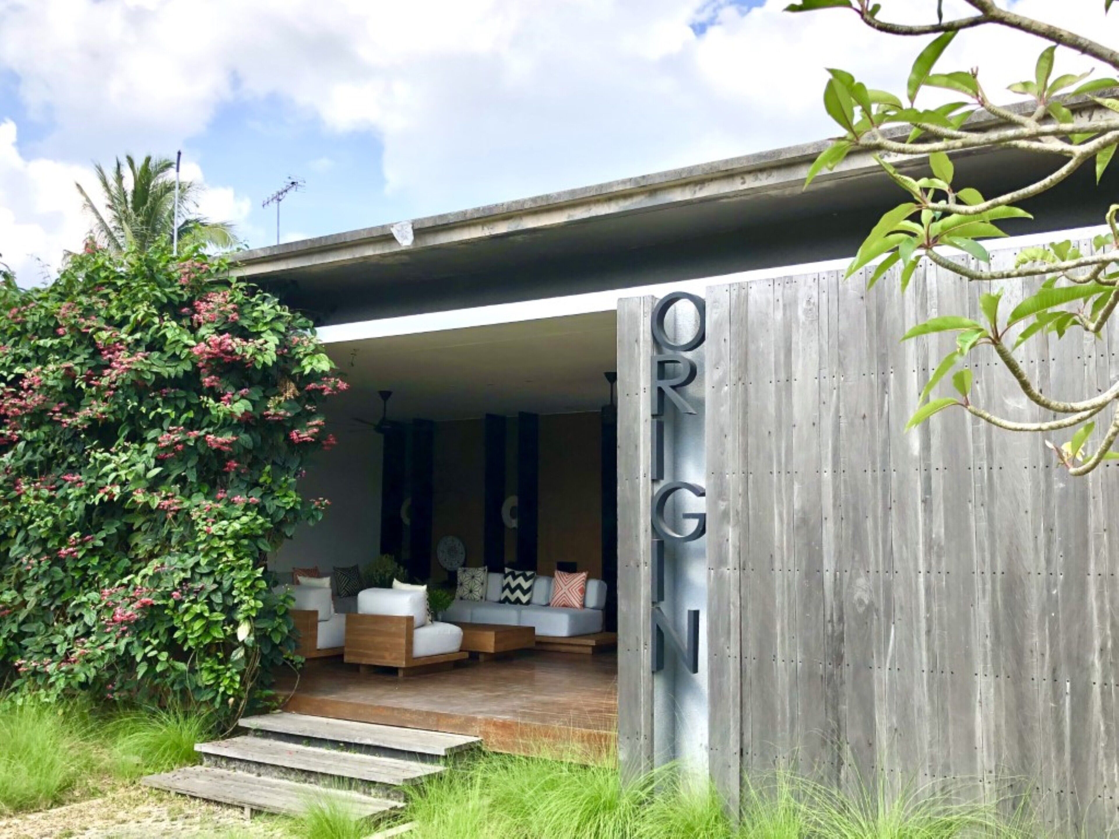 Een modern huis met een houten gevel en een overdekt terras met banken en kussens.