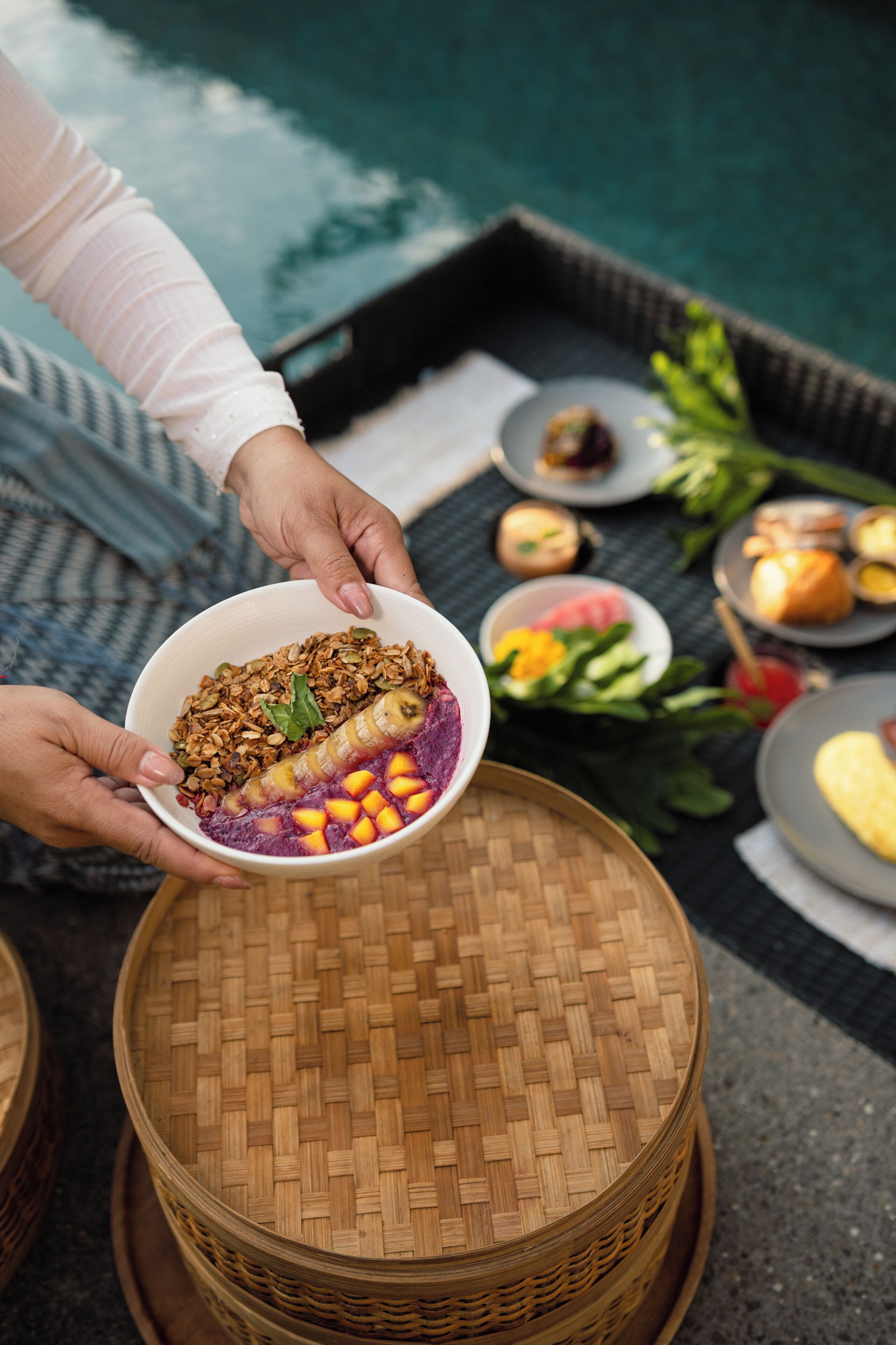A person holding a bowl of food near a table with various dishes and a woven basket.