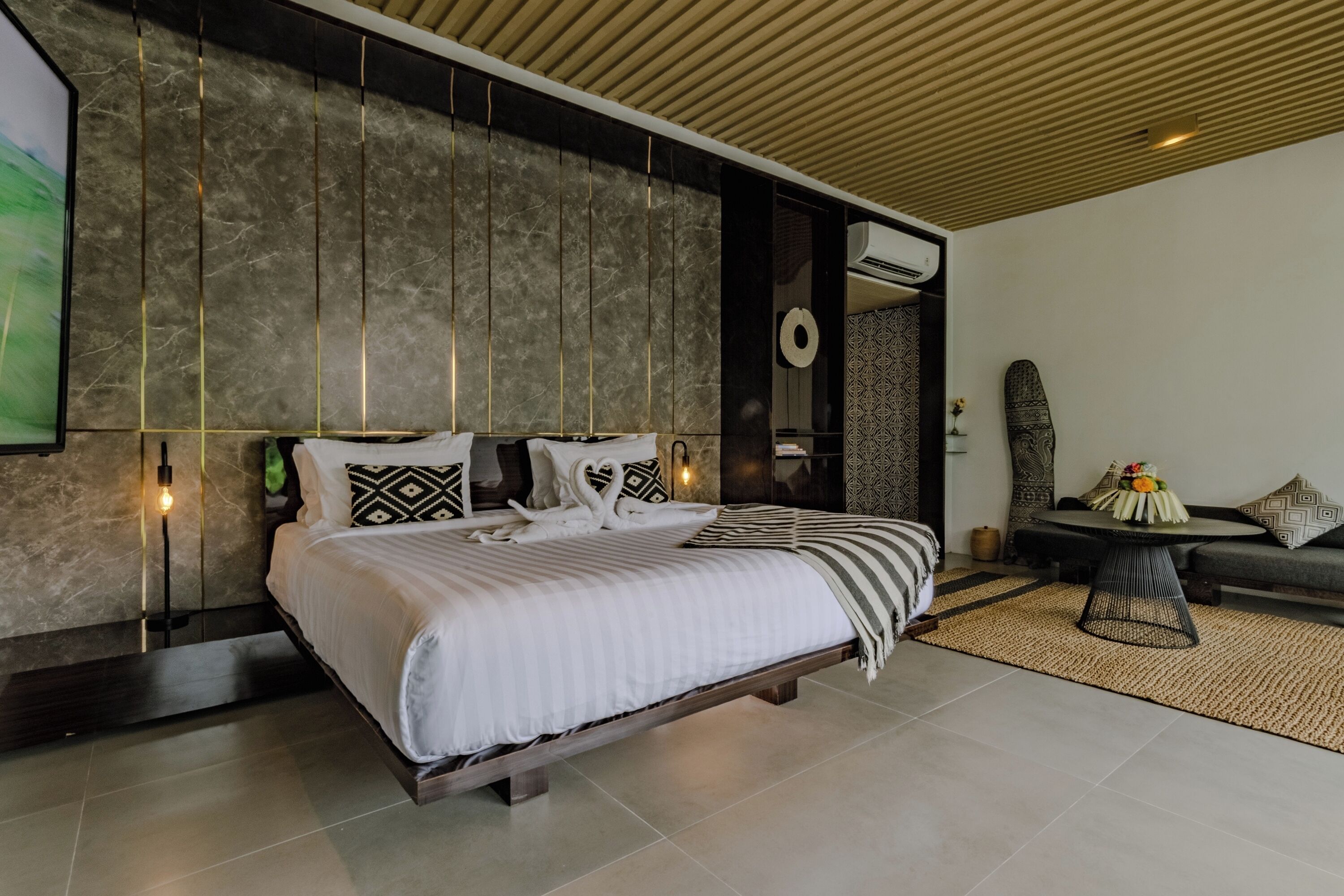 Un dormitorio moderno con una cama grande, techo de madera y pared con estampado.