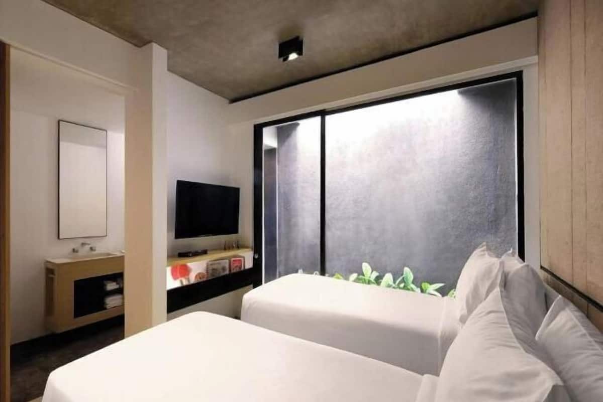 A modern hotel room with a bed, a TV, a large window, and a small bedside table.