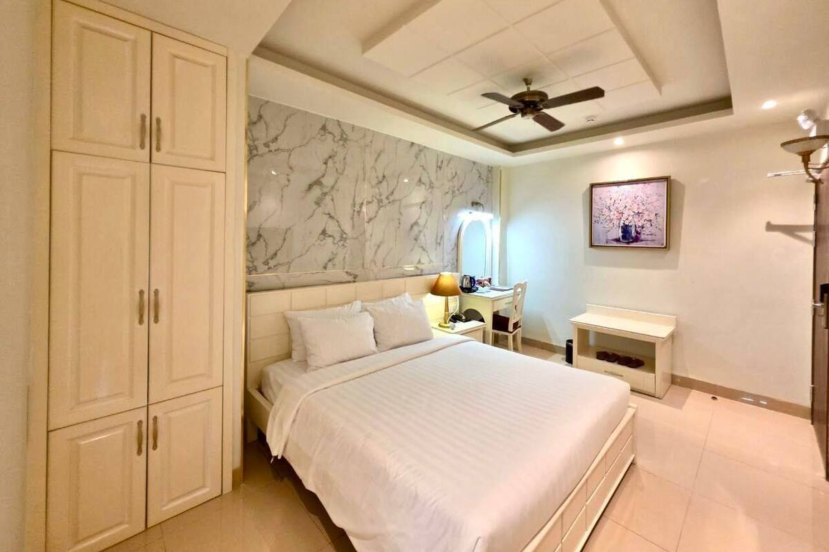 A bedroom with a bed, a desk, a chair, a wardrobe, and a ceiling fan.
