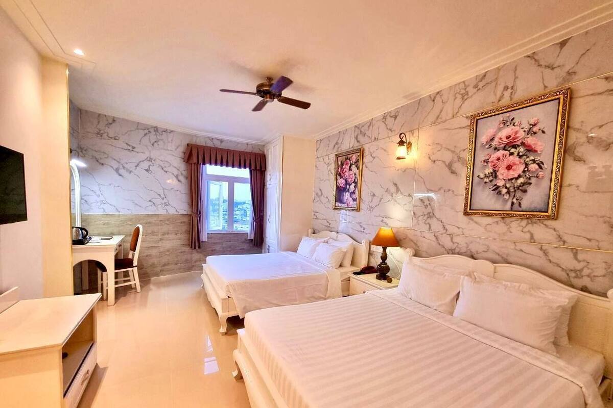 A hotel room with two beds, a desk, a chair, a ceiling fan, and a window with curtains.