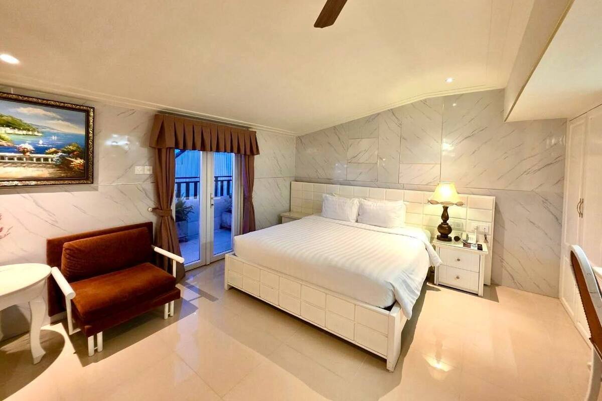 A modern hotel room with a large bed, a seating area, and a view of the outside.