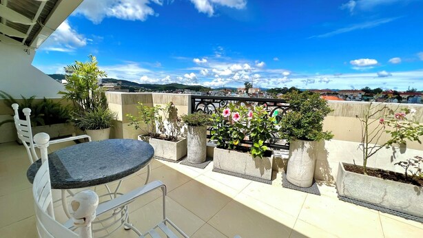 A rooftop terrace with a table and chairs, surrounded by potted plants and flowers, offering a view of the cityscape. - Tulip Hotel 3 (Xuan Huong - Da Lat)