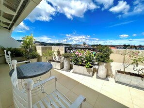 Eine Dachterrasse mit Tisch und Stühlen, umgeben von Blumentöpfen und Blumen, mit Blick auf die Stadt.
