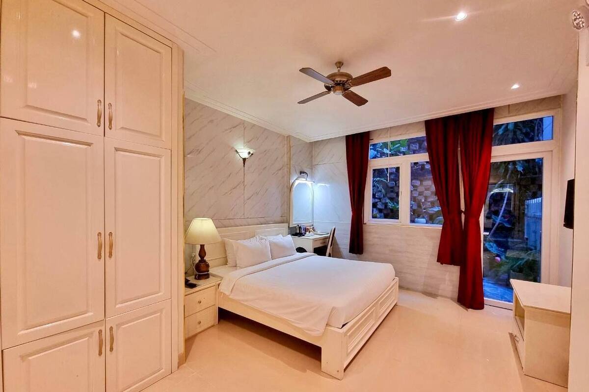 A bedroom with a bed, nightstands, a desk, a ceiling fan, and a window with curtains.