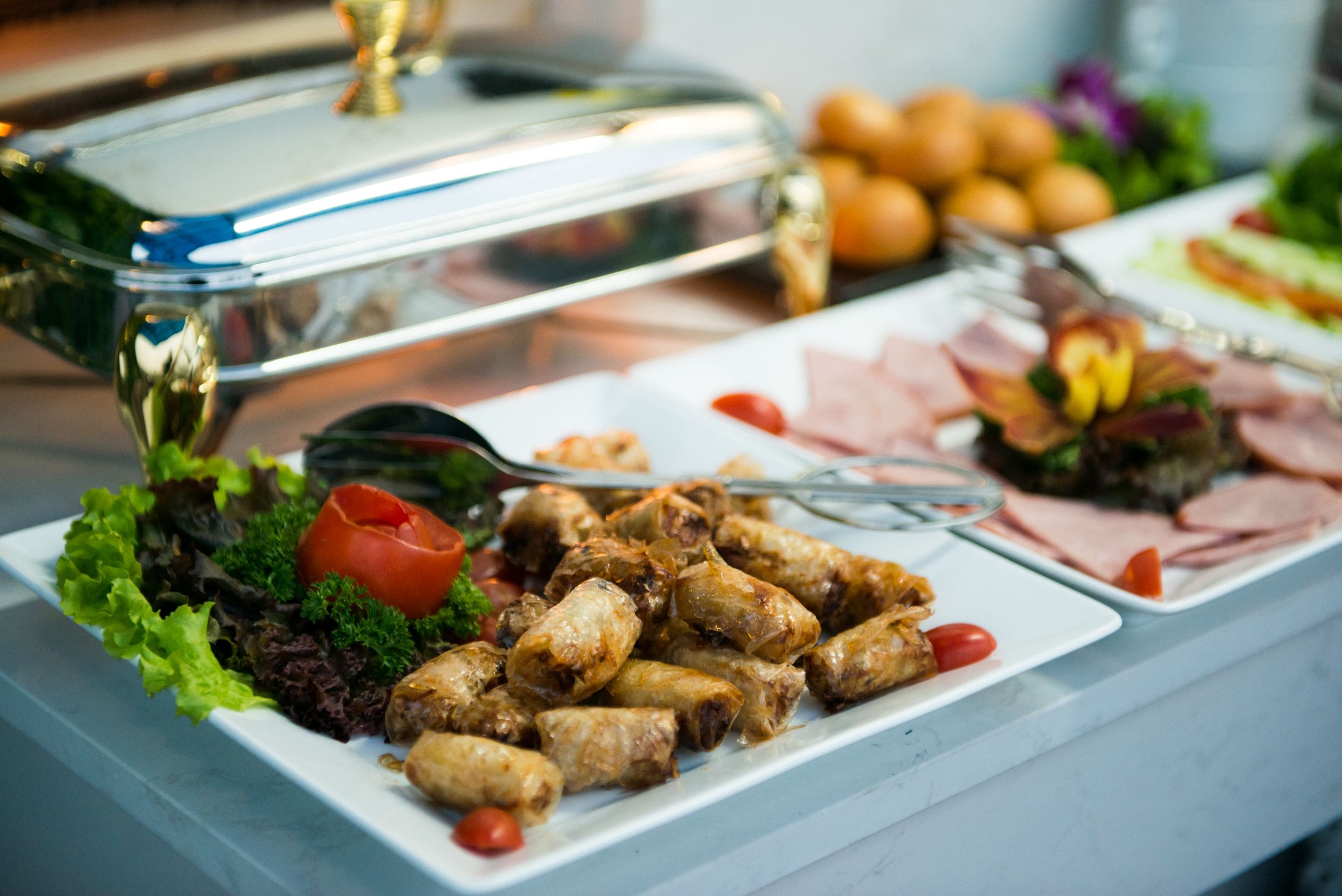 A buffet table with various dishes including spring rolls, salads, and meats.
