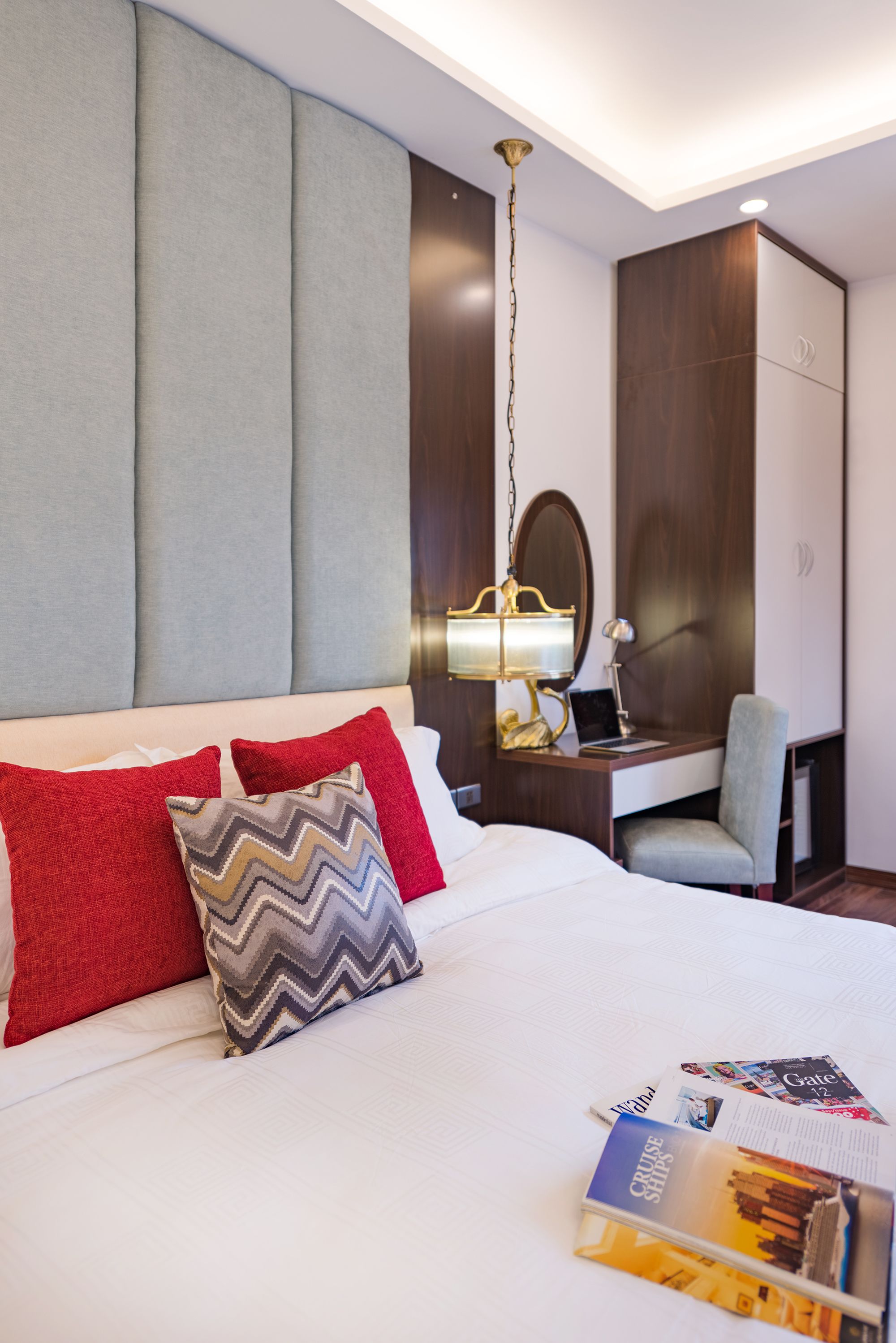 A hotel room with a bed, a desk, a chair, and a lamp.