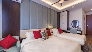 Habitación de hotel con dos camas, un escritorio, una silla, un ventilador de techo y un espejo redondo en la pared.