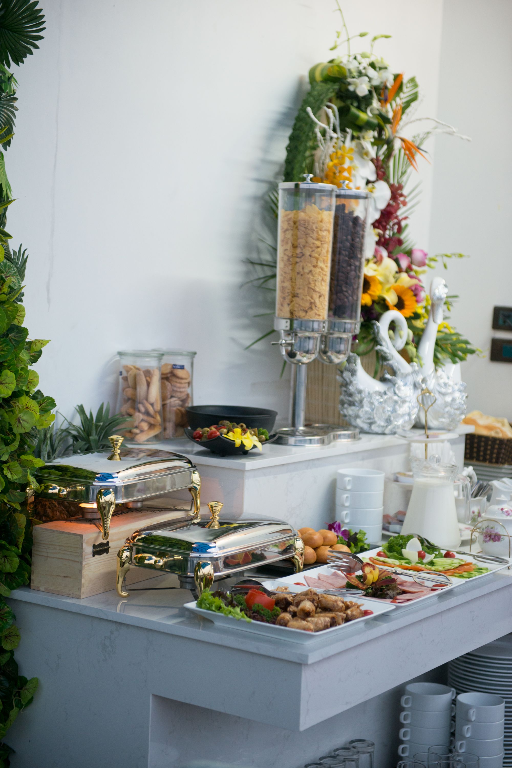 A buffet table with various food items, a decorative swan, and a vase of flowers.