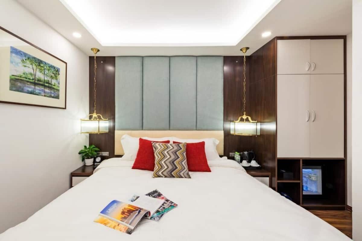 A hotel room with a bed, bedside lamps, a TV, and a wardrobe.