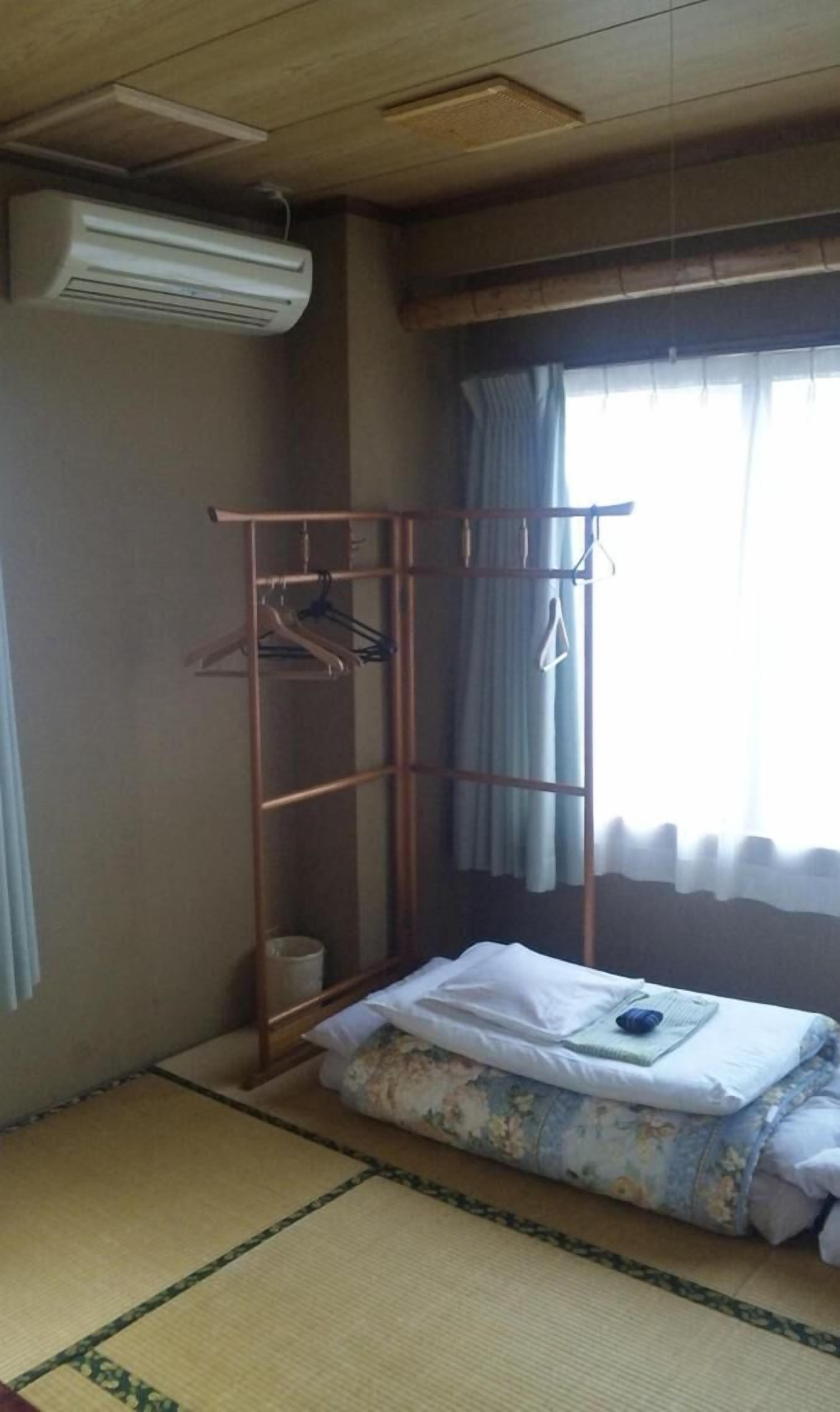 A room with a futon bed, a metal drying rack, and a window with curtains.