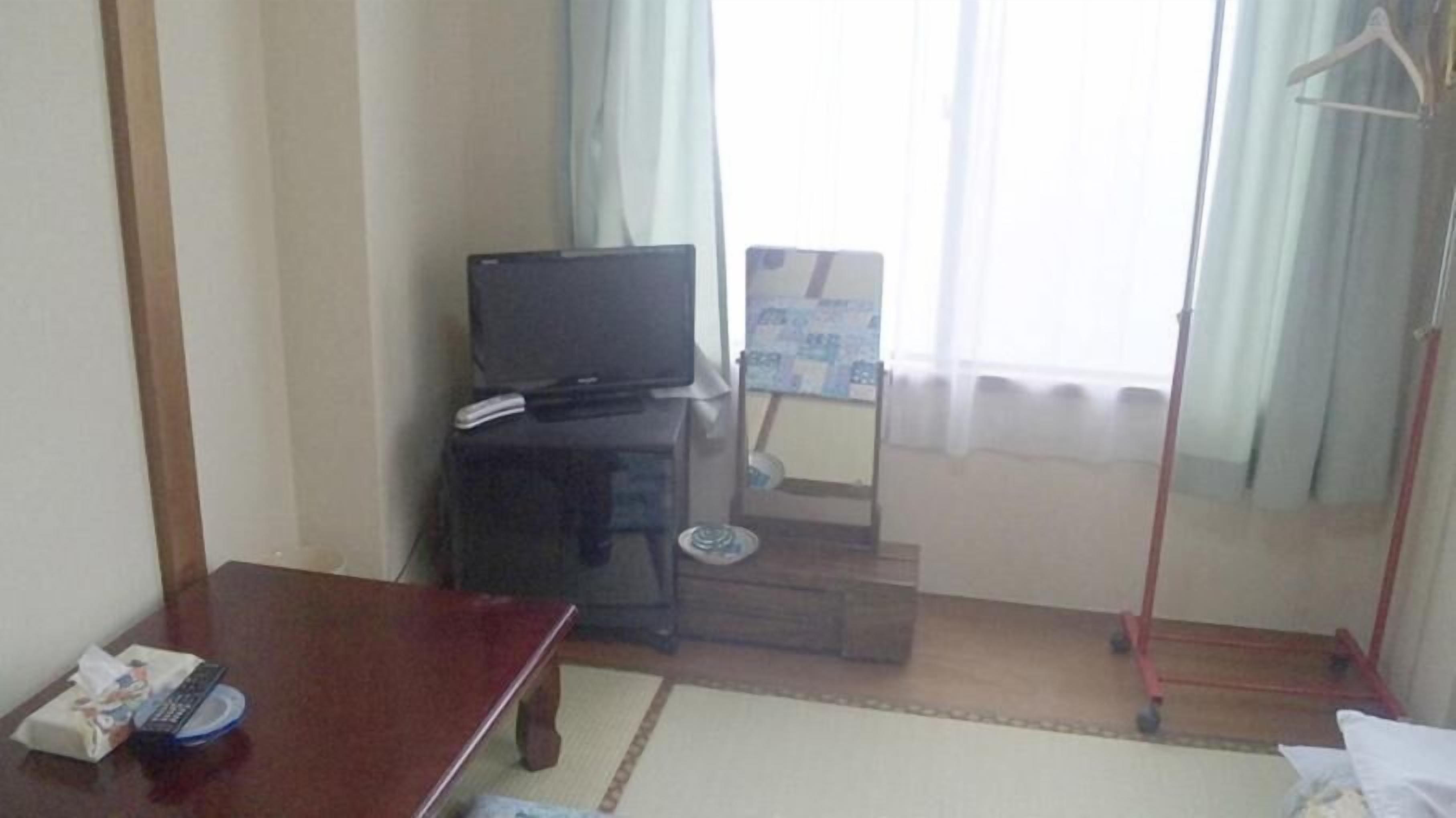 A hotel room with a television, a small table, a chair, a bed, and a window with curtains.