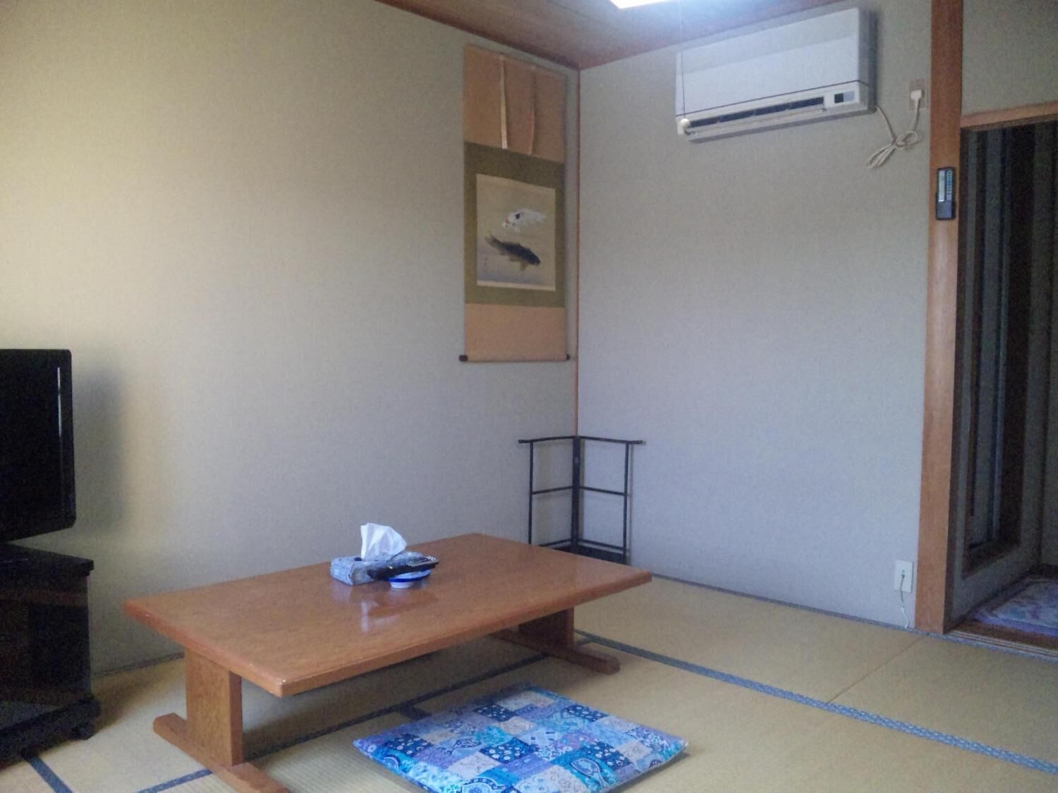 A small room with a wooden table, a tatami mat, a wall-mounted air conditioner, and a framed picture.