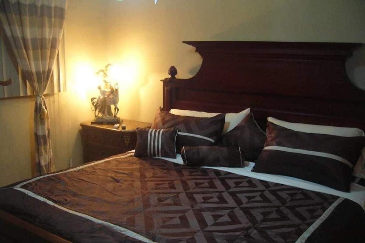 A neatly made bed with a patterned bedspread, a wooden headboard, and a bedside table with a lamp and a decorative item.