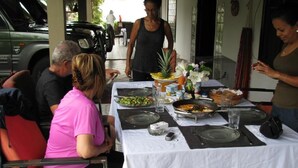 A dining table set outdoors with various dishes, a pineapple, and a woman standing behind it.