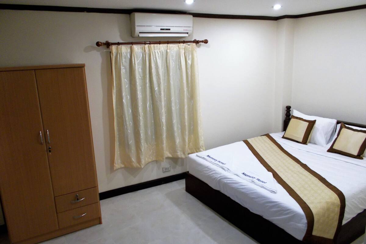 A hotel room with a bed, a wardrobe, a curtain, and an air conditioning unit.