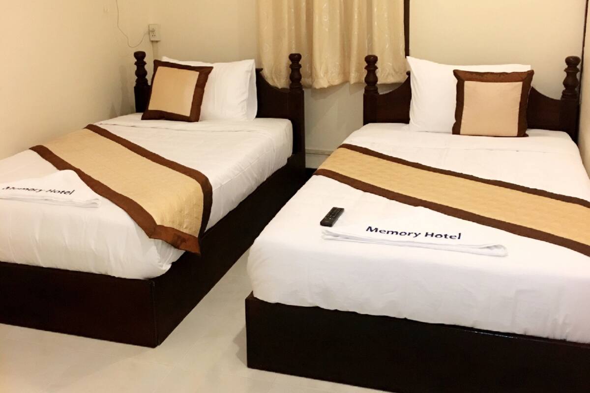 A hotel room with two beds, each with a brown and white bedspread, a remote control, and a sign indicating the hotel name.