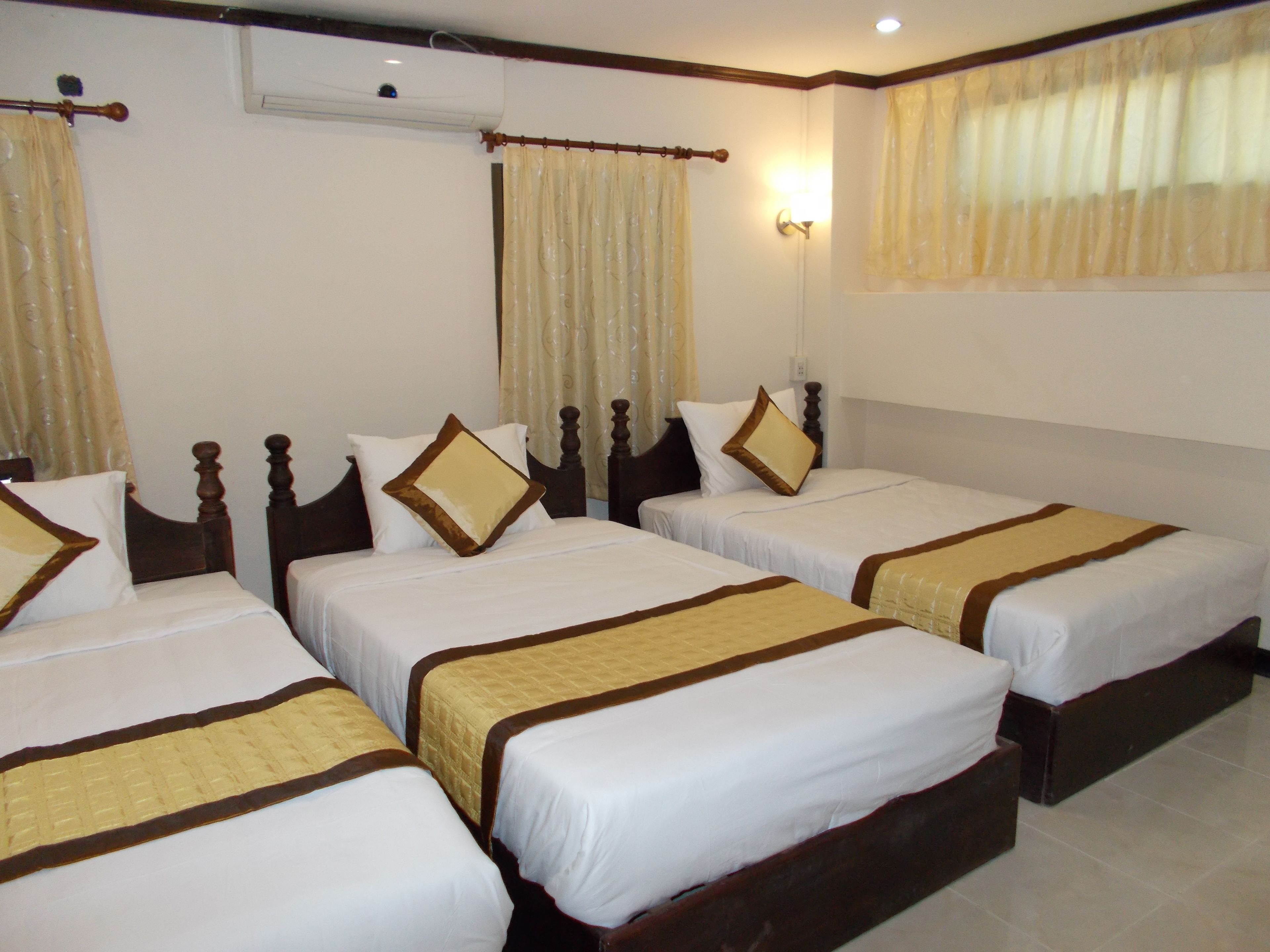 A hotel room with four single beds, each with a wooden headboard and a quilted bedspread.