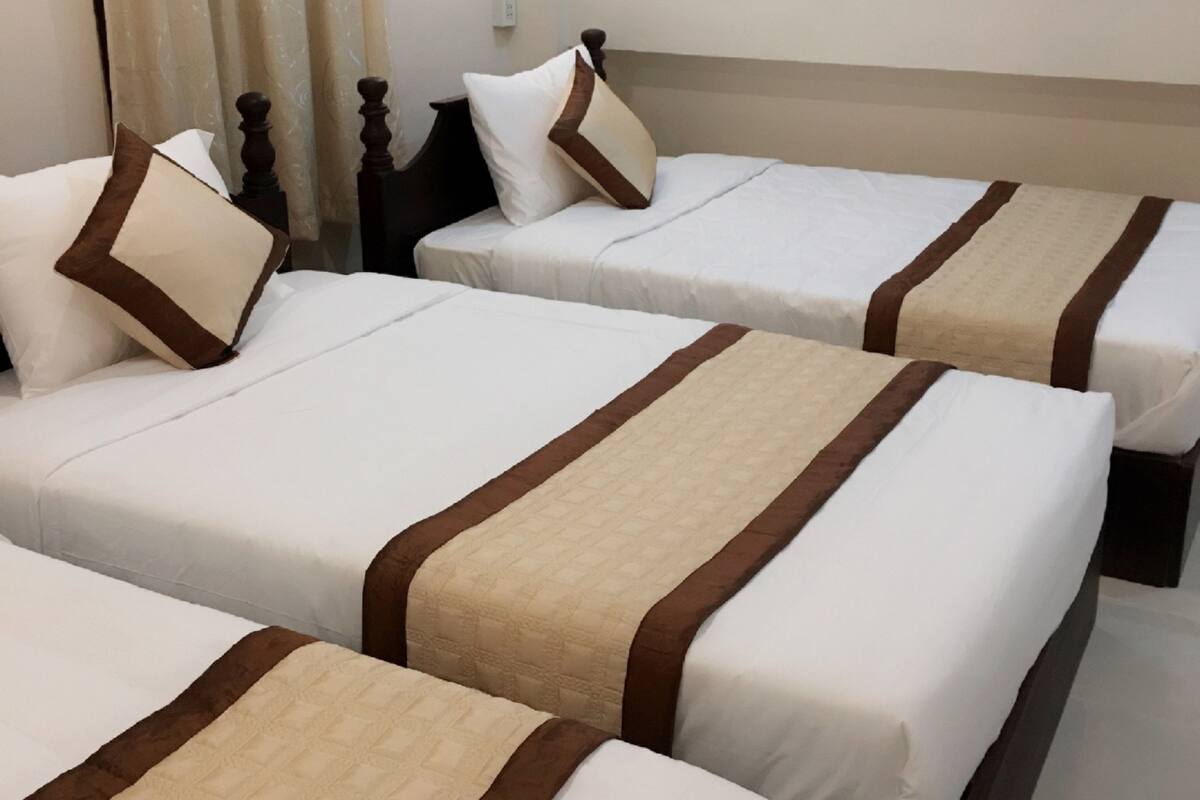 A hotel room with three single beds, each with a brown and beige bedspread, white pillows, and a wooden headboard.