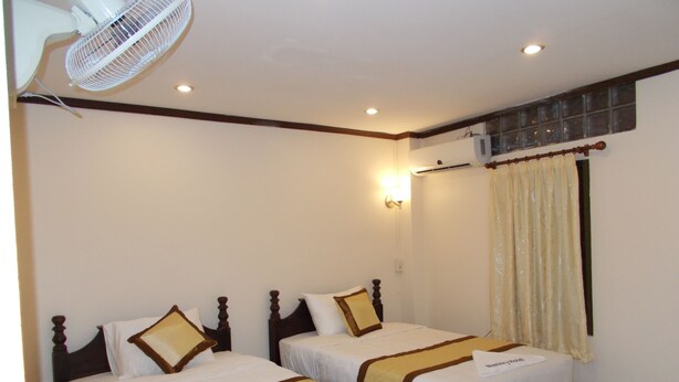 A hotel room with two single beds, a ceiling fan, an air conditioning unit, and a window with curtains. - Memory Hotel (Vientiane)
