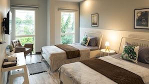 Habitación de hotel con dos camas, un escritorio y una silla. Ventanas con vistas a zonas verdes.