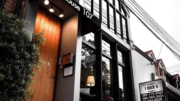 Un edificio moderno con un cartel que indica 'House 107' y un letrero de alquiler con datos de contacto.