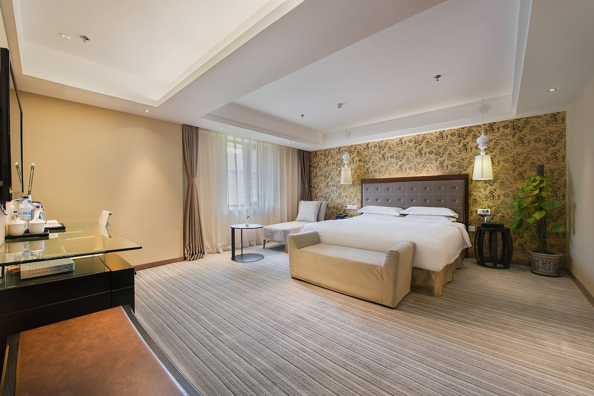 A hotel room with a large bed, a desk with a computer, a chair, and a small table.