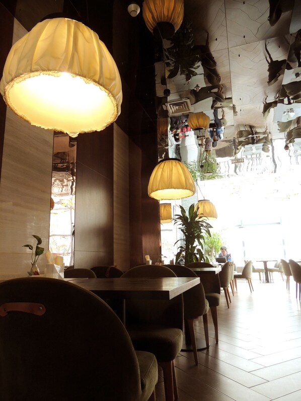 Interior de restaurante con mesas y sillas de madera, lámparas amarillas colgantes y un amplio ventanal que deja entrar luz natural.