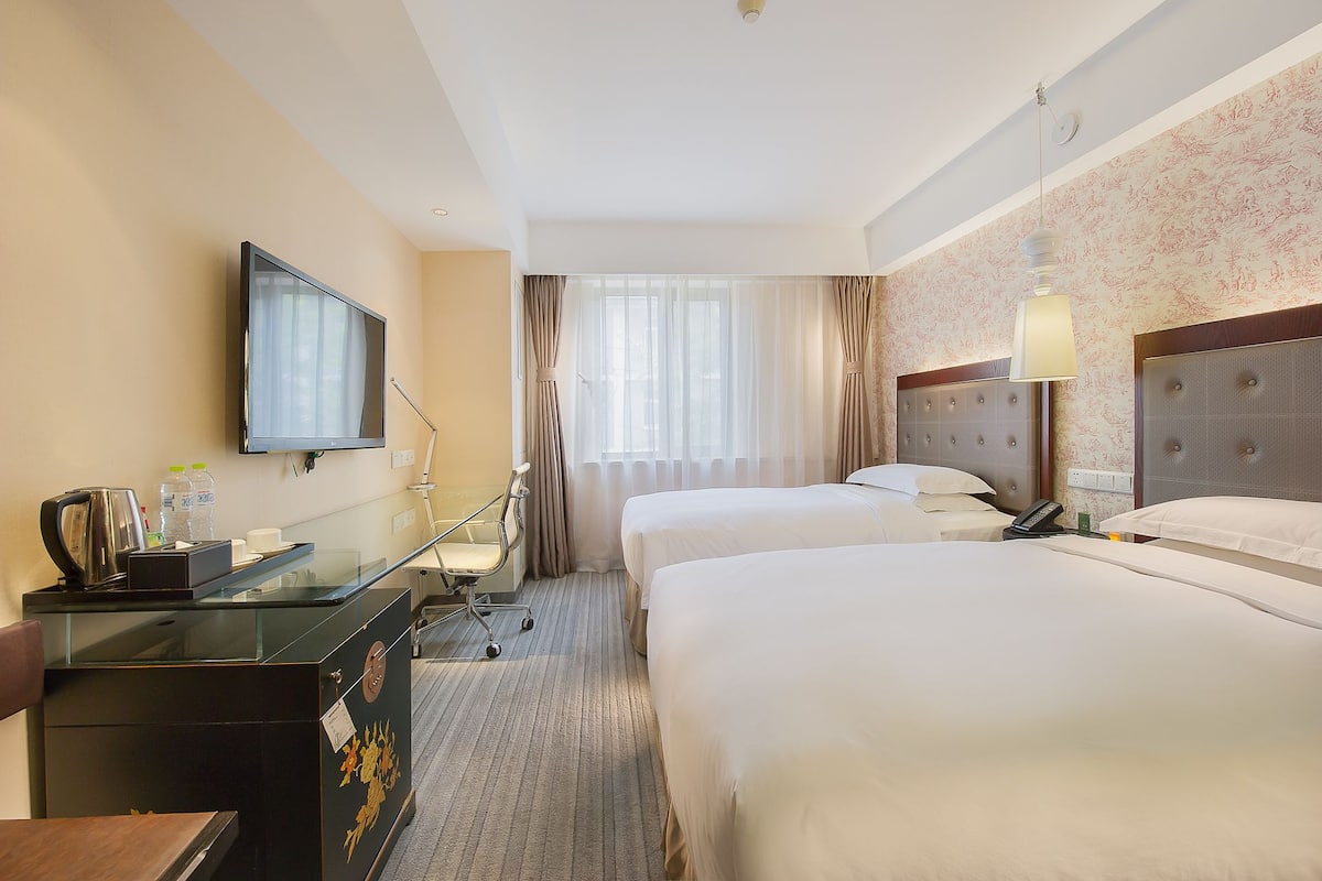 A hotel room with two beds, a desk with a chair, a television, and a window with curtains.
